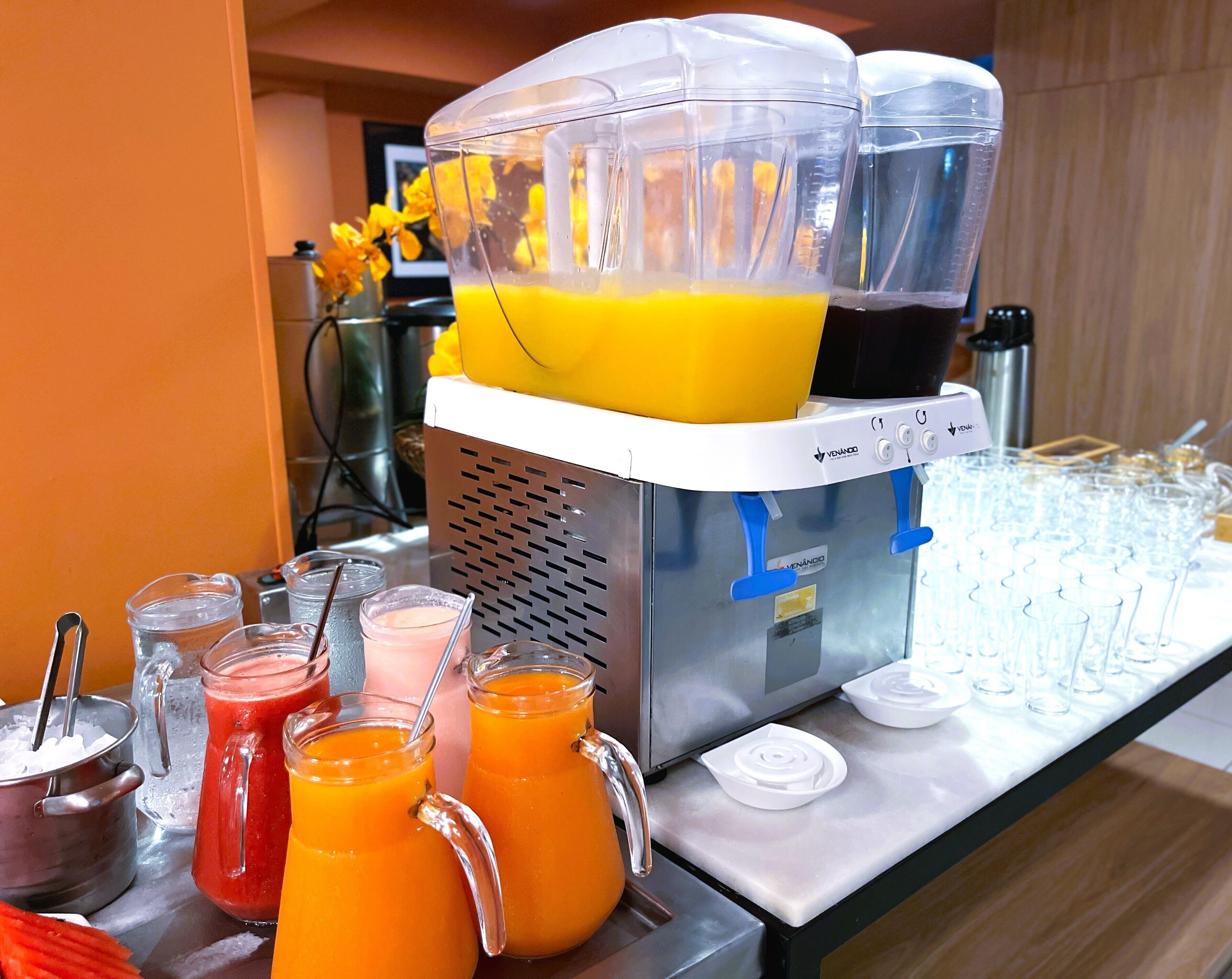Un bar con frullatore e diversi contenitori di vetro riempiti con succhi di vari colori.