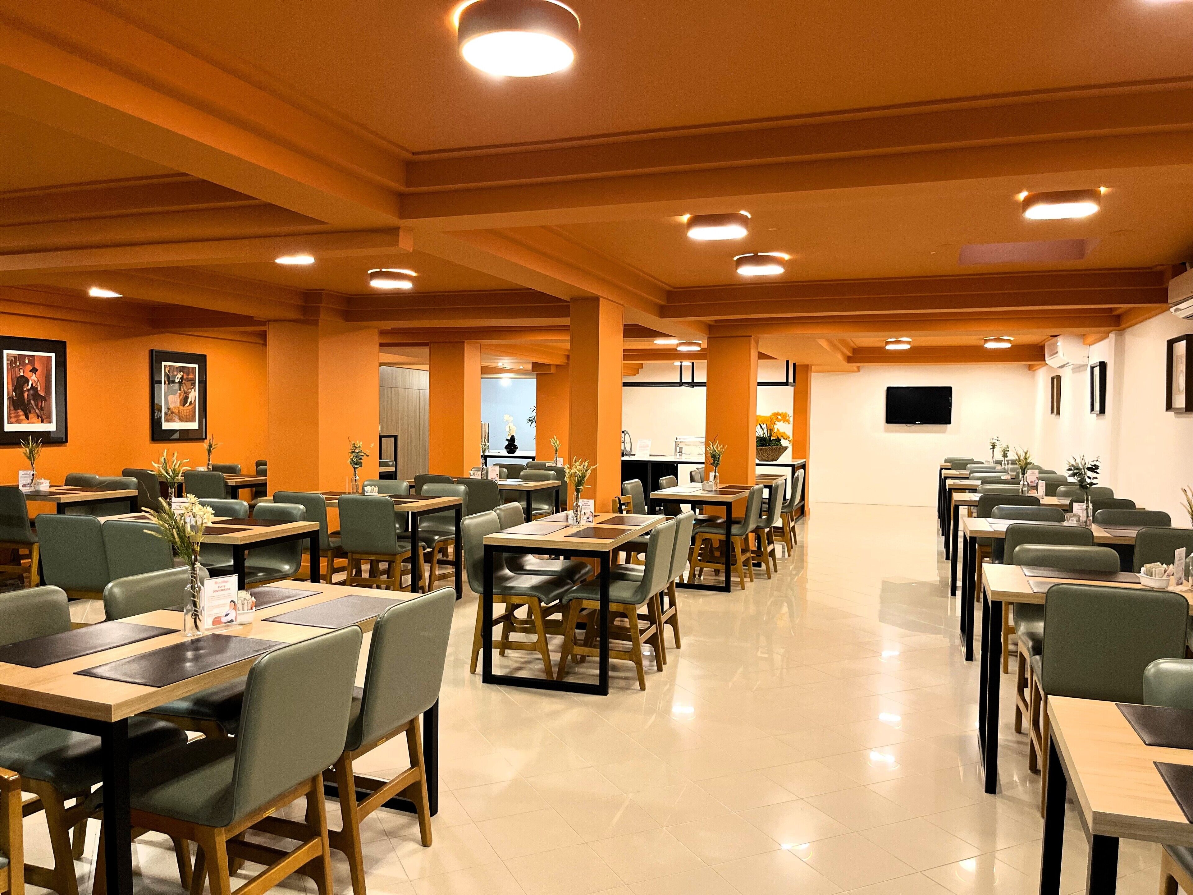 A spacious dining area with multiple tables and chairs, a flat-screen TV mounted on the wall, and framed artwork on the walls.