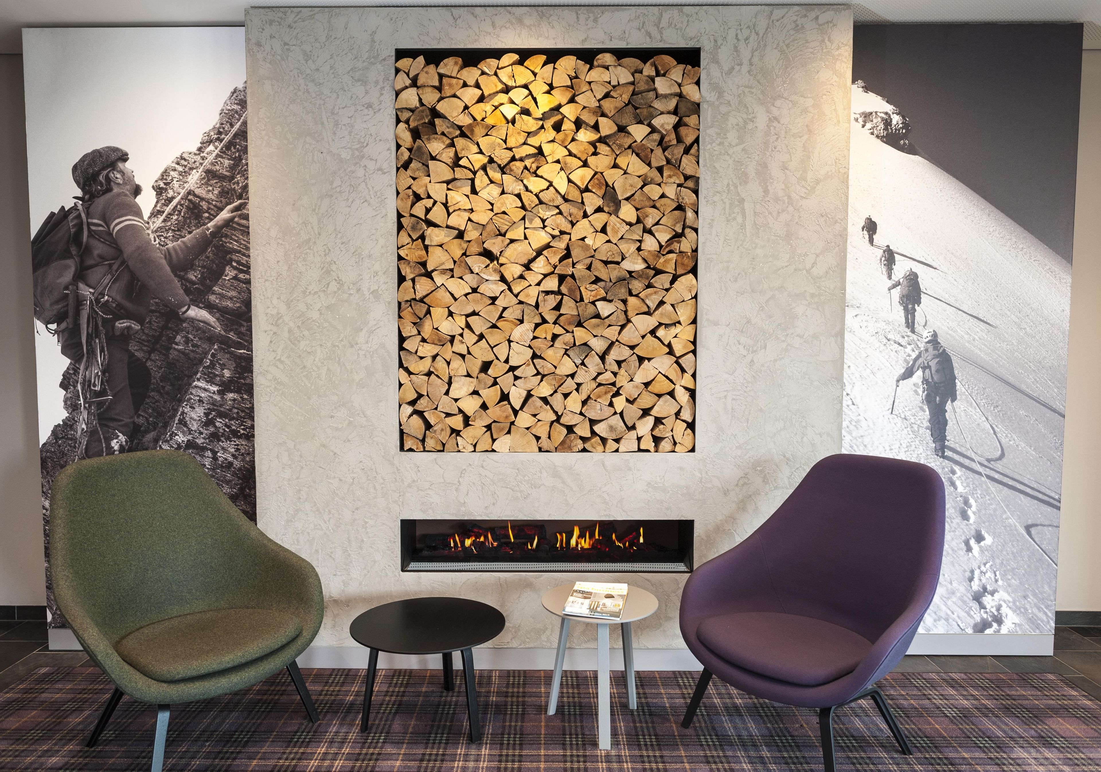 A room with a fireplace, two chairs, a small table, and two large wall art pieces.
