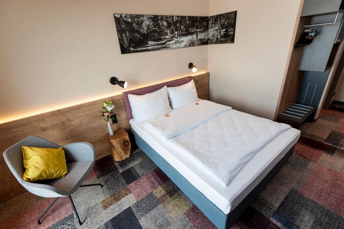A modern hotel room with a large bed, a small seating area, and a wall-mounted artwork.