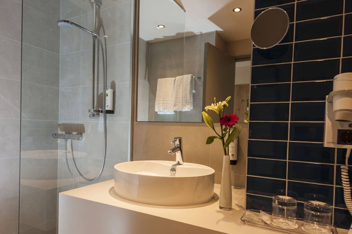 A modern bathroom with a glass-enclosed shower, a round sink, and a large mirror.