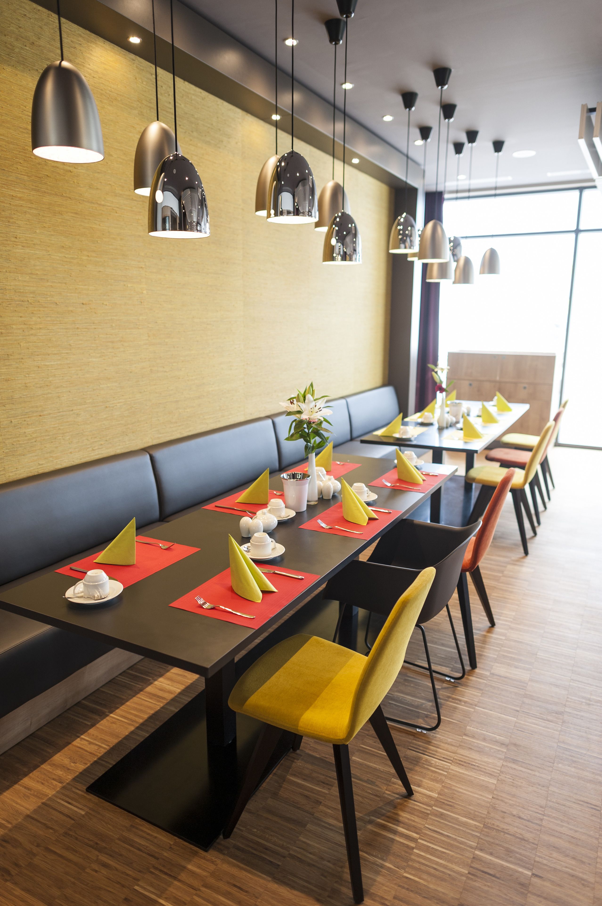 A modern restaurant with a long table set for dining, featuring yellow chairs and red placemats.