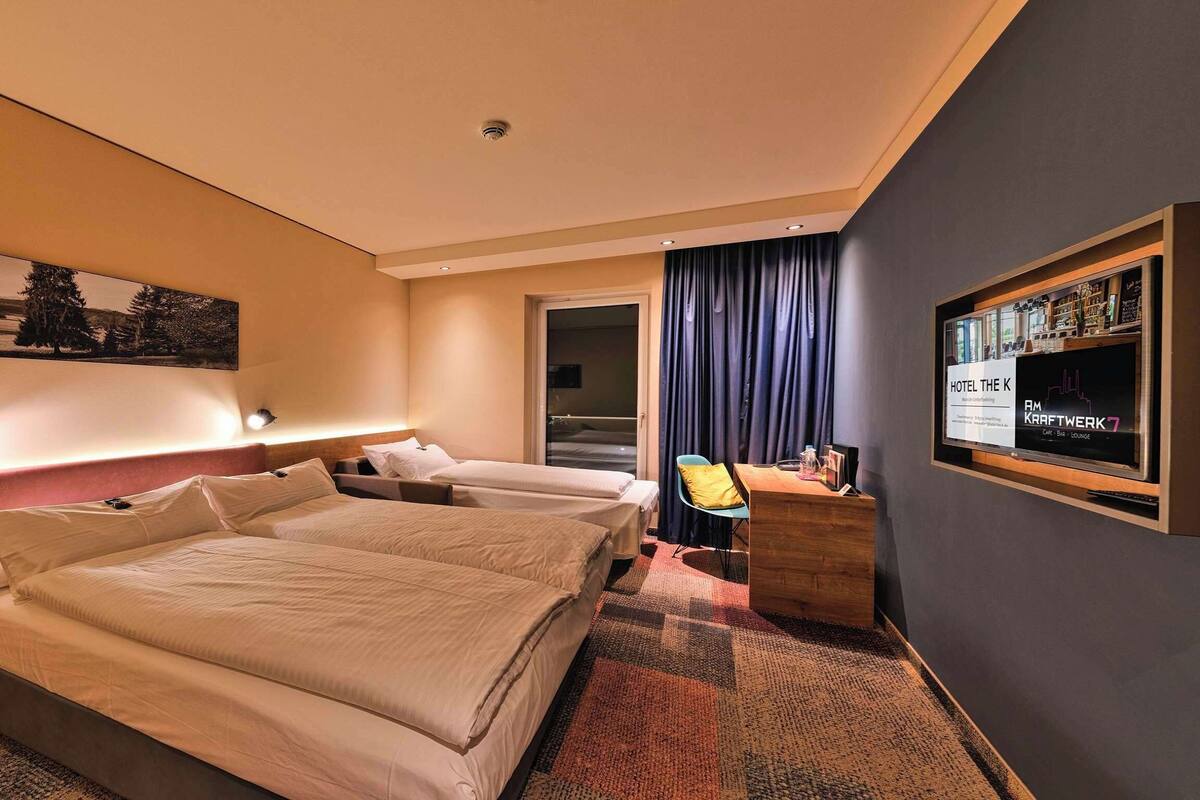 A hotel room with two beds, a desk, a chair, a TV, and a painting on the wall.