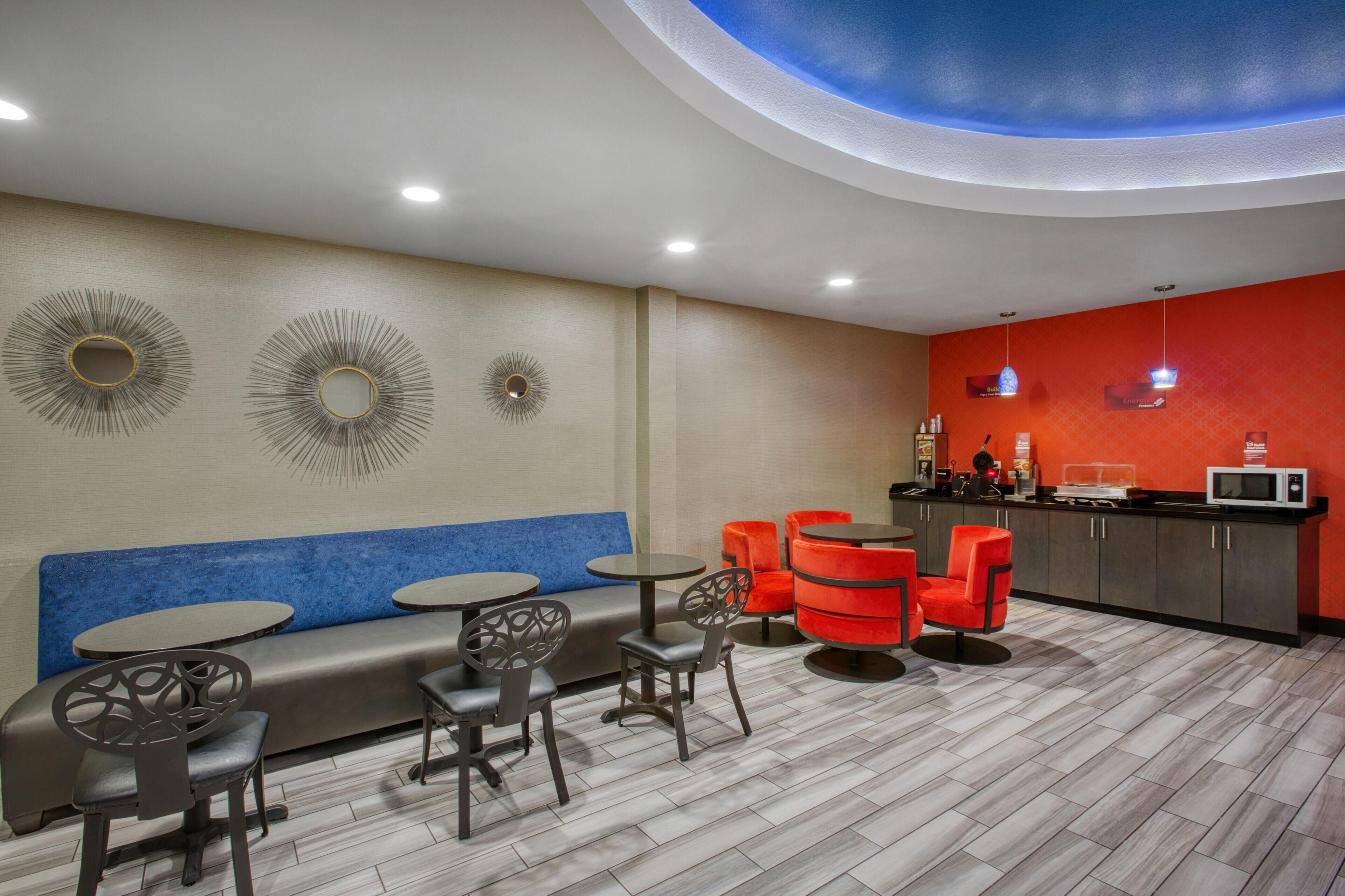 A modern lounge area with a blue sofa, round tables, and red chairs.