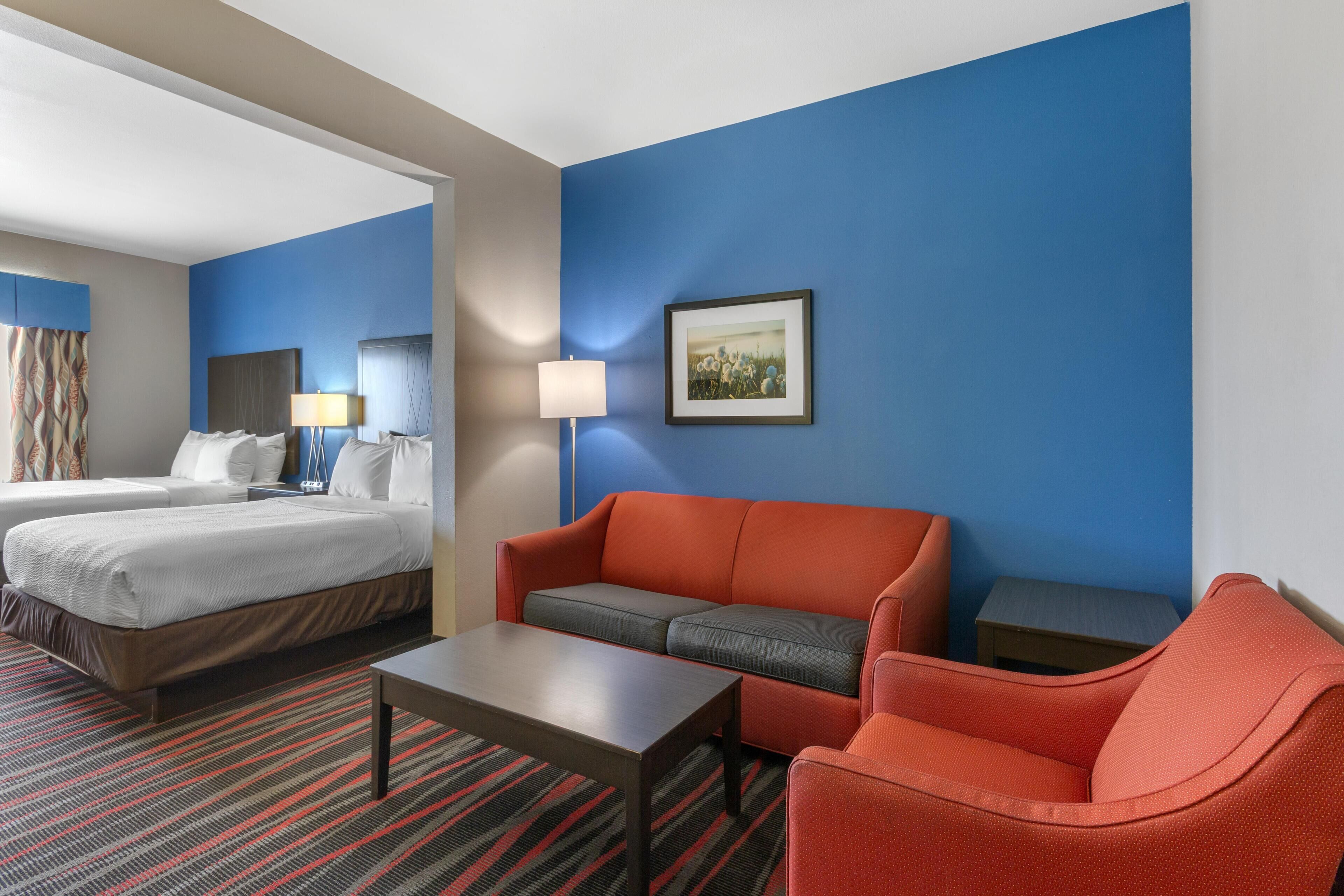 A hotel room with a bed, a sofa, a coffee table, and a small table with a lamp.