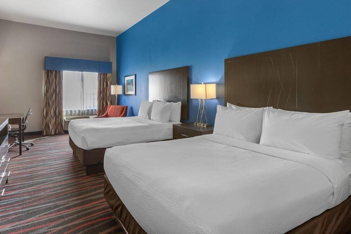A hotel room with two beds, a desk, a chair, and a window with curtains.