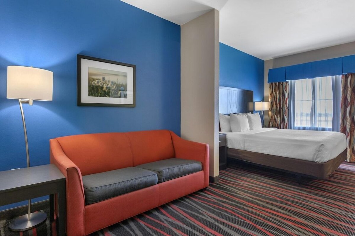 A hotel room with a bed, a sofa, a desk, and a framed picture on the wall.