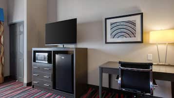 Habitación de hotel con televisión de pantalla plana en un mueble, un escritorio con una silla, un cuadro en la pared y una lámpara.