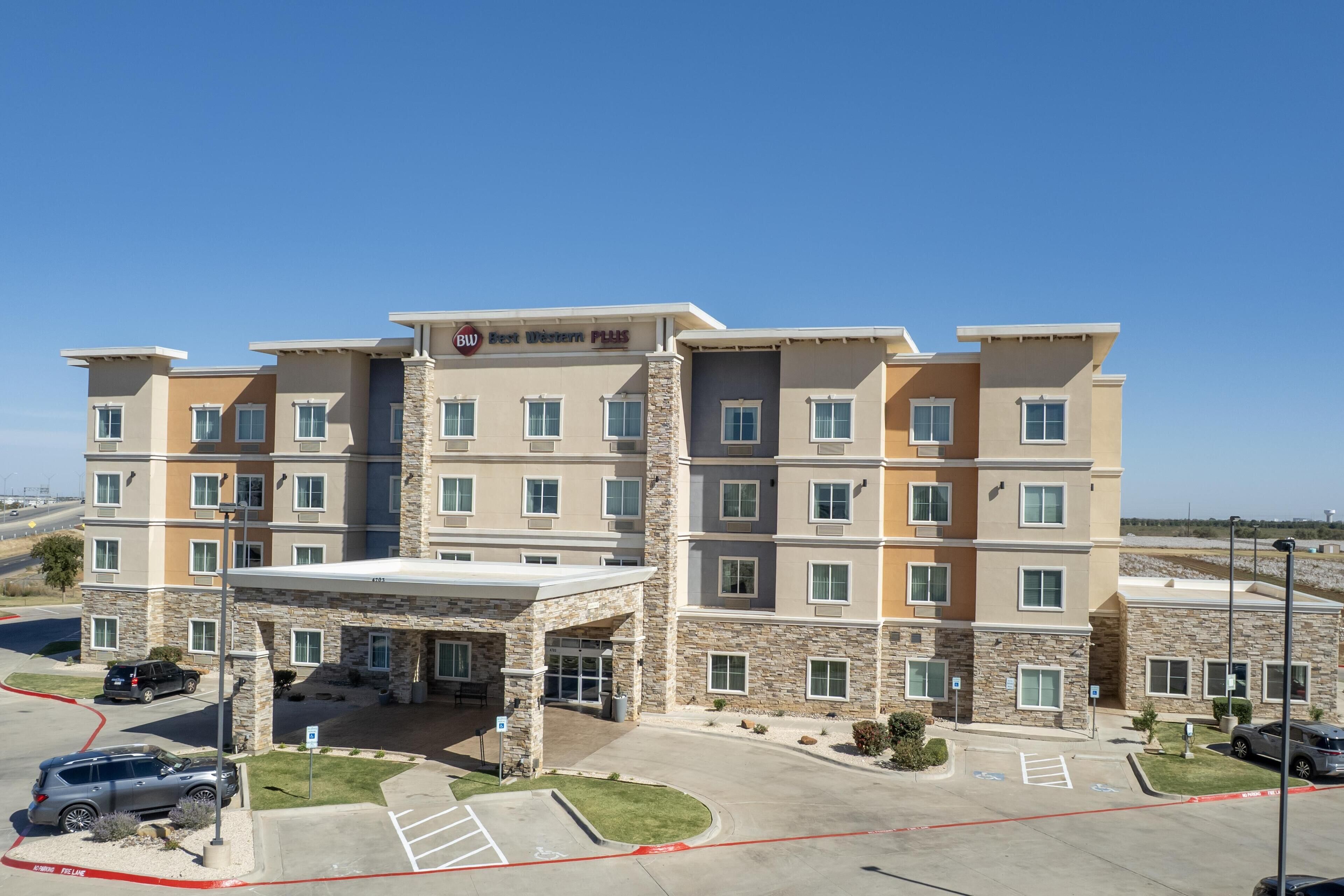 A multi-story hotel with a stone facade, a covered entrance, and a parking lot with marked spaces.