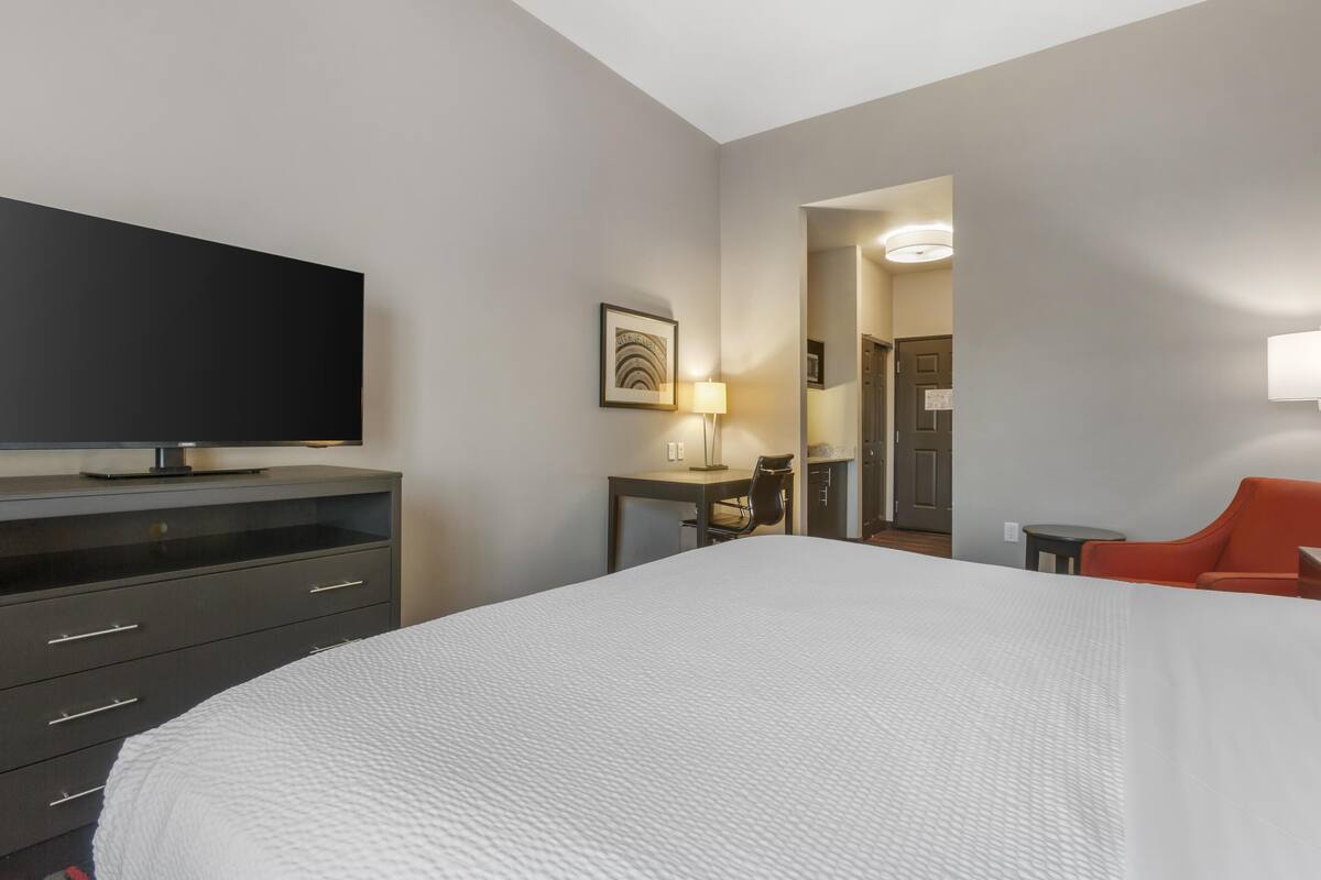 A hotel room with a large bed, a flat-screen TV on a dresser, a desk with a lamp, and a chair.