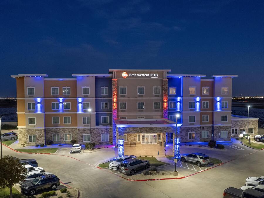 A multi-story hotel with a sign reading "Best Western PLUS" and a parking lot with several cars.