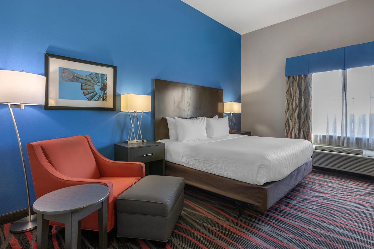 A hotel room with a bed, a chair, a small table, and a framed picture on the wall.