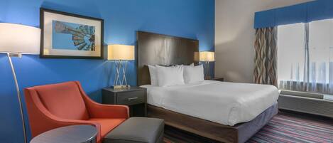 A hotel room with a bed, a chair, a small table, and a framed picture on the wall.