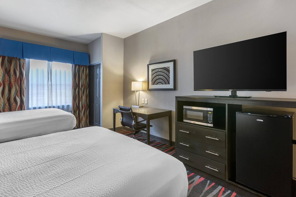 A hotel room with two beds, a desk with a chair, a television, a microwave, and a refrigerator.