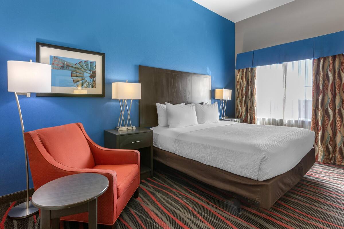 A hotel room with a large bed, a red armchair, a small table, two bedside lamps, and a framed picture on the wall.