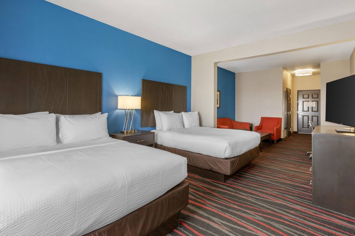 A hotel room with two beds, a desk, a chair, and a TV.