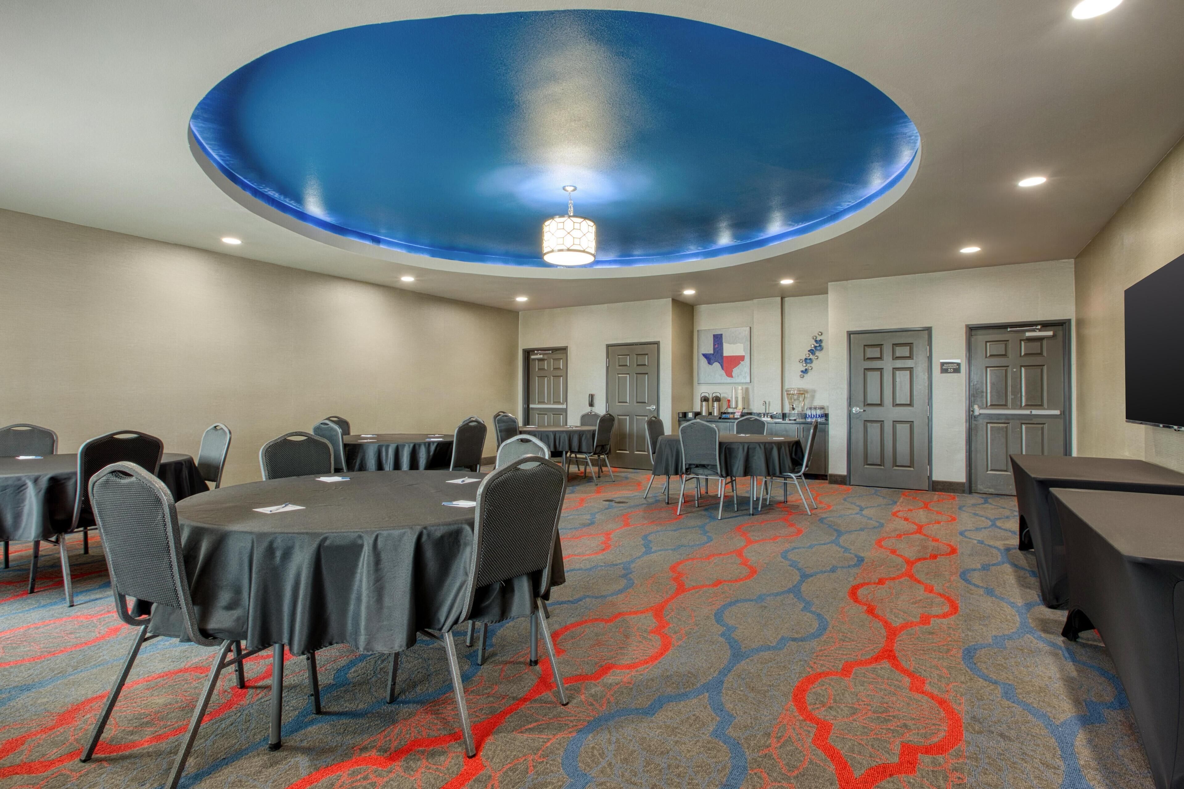 A conference room with round tables, chairs, and a blue ceiling design.