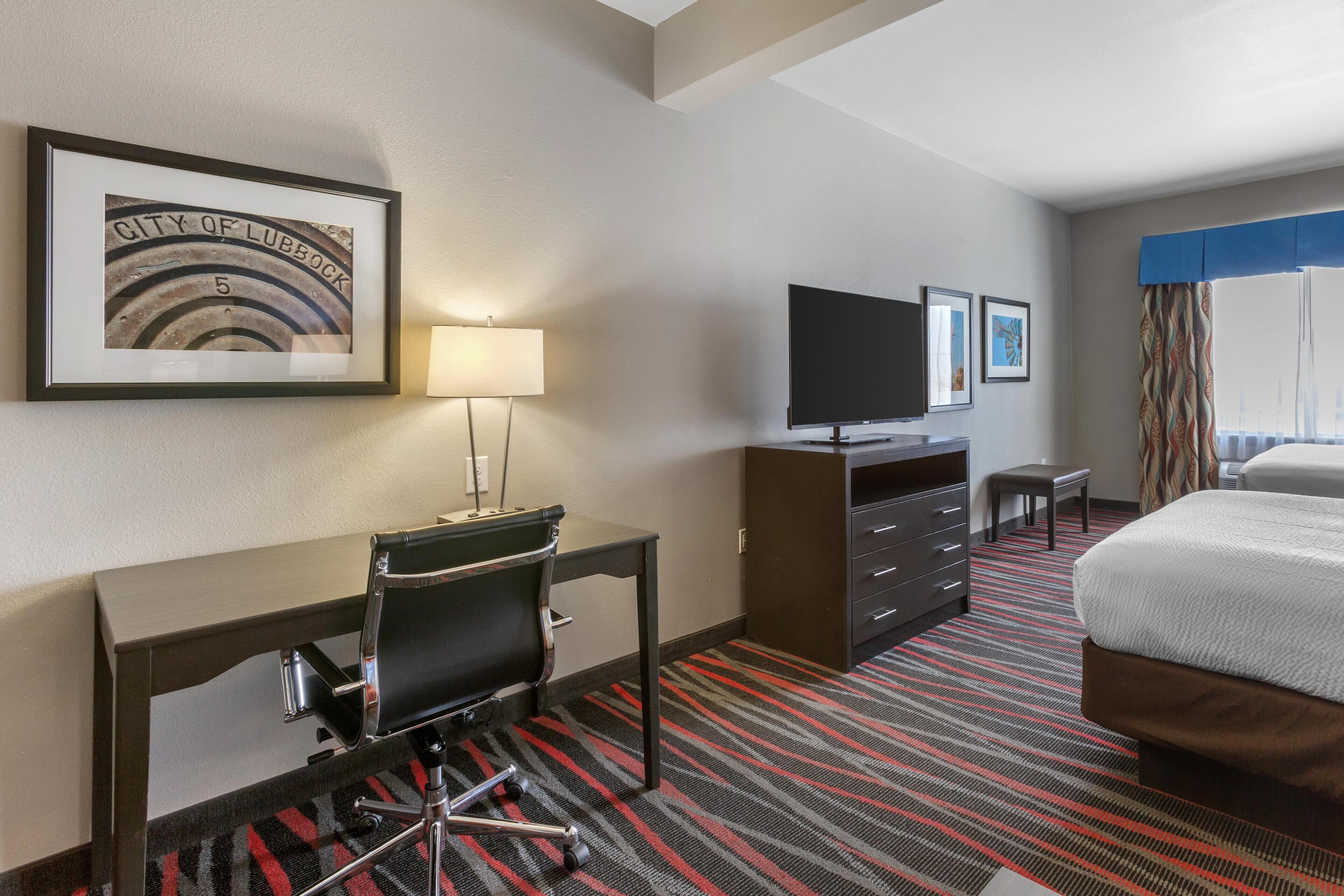 A hotel room with a desk, chair, television, bed, and a framed picture on the wall.