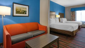 Een hotelkamer met een blauwe muur, een ingelijst kunstwerk, een rode bank, twee bedden, een nachtkastje en een lamp.