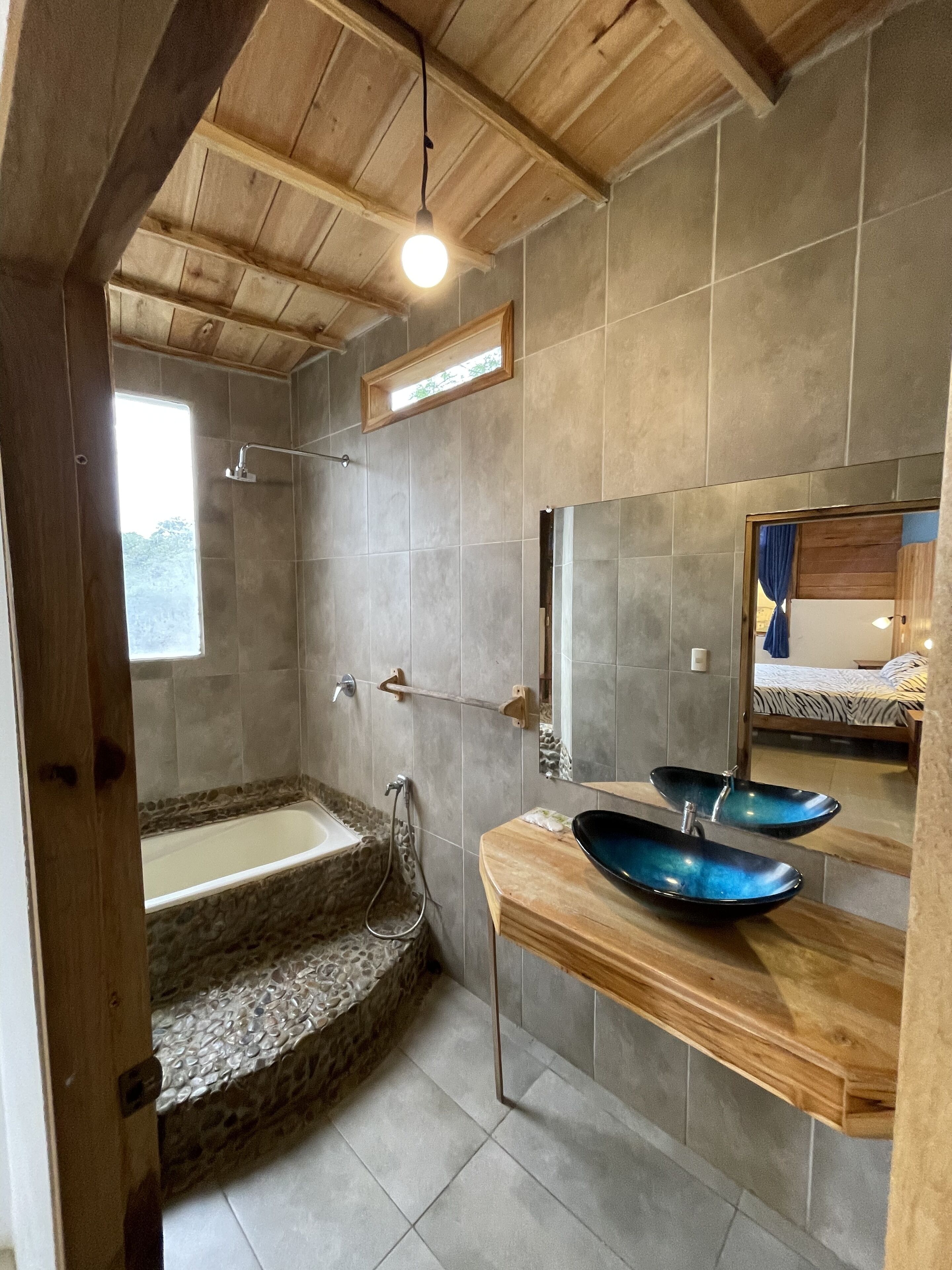 A bathroom with a stone bathtub, a wooden vanity with a blue basin, and a large mirror.