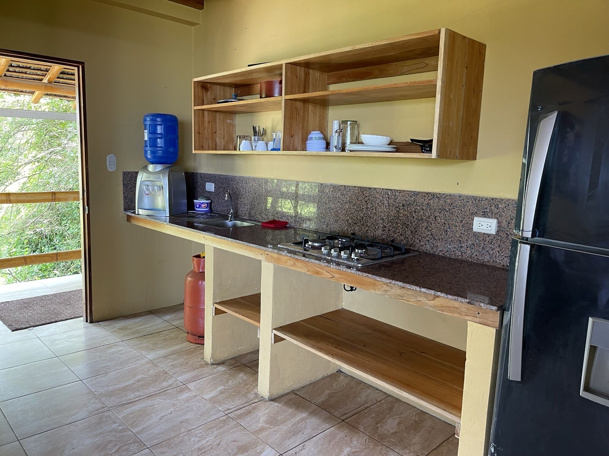 Una cocina con encimera de granito, armarios de madera, estufa a gas y refrigerador negro.