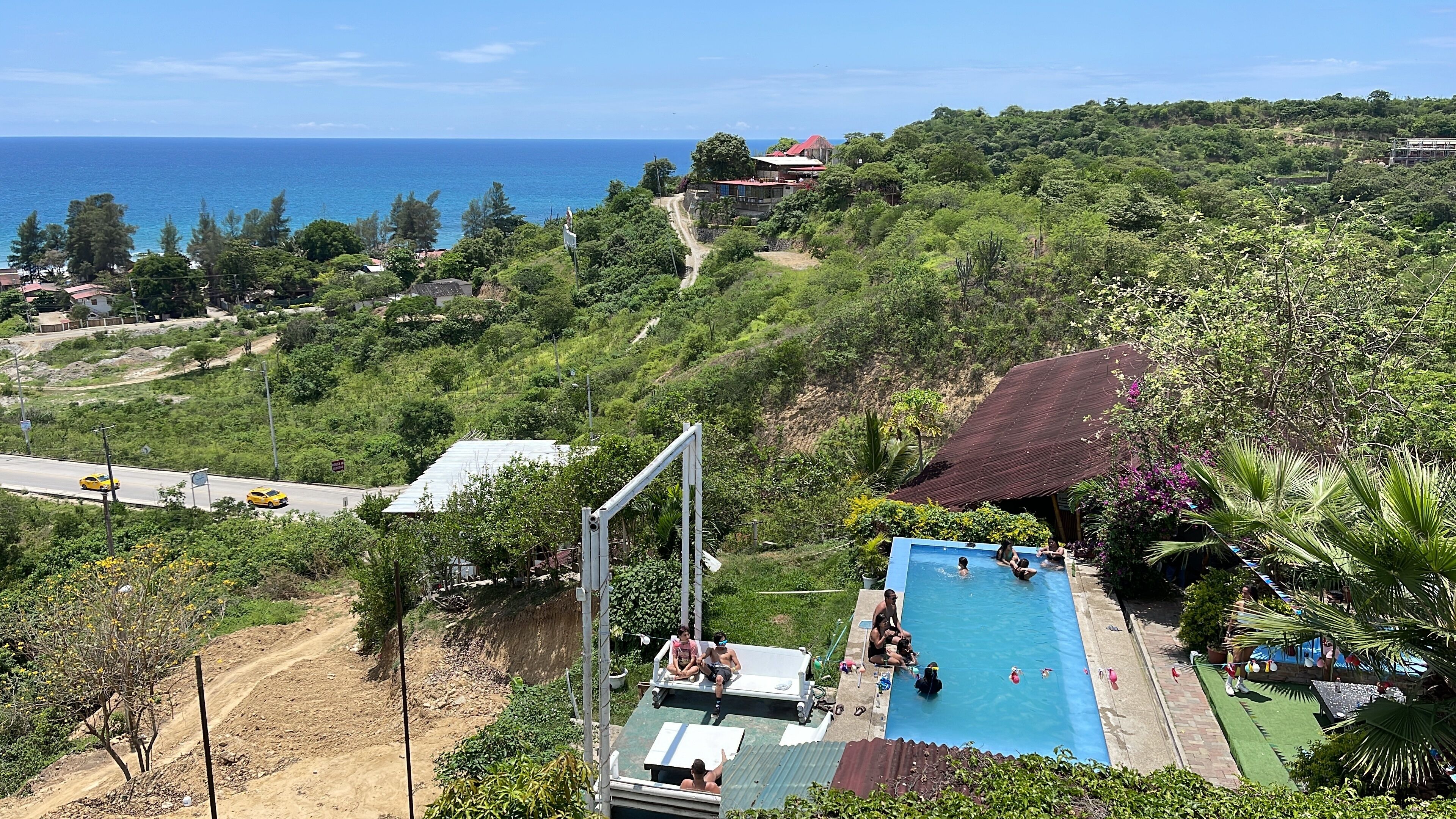 A pool area with a view of the ocean, surrounded by lush greenery and a hilly landscape.