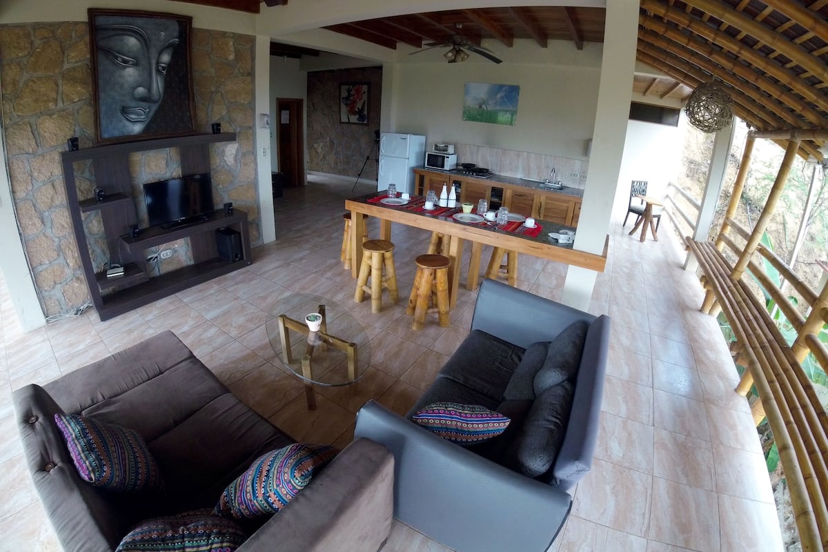 Un vaste espace de vie agrémenté d’un mur en pierre, d’une cheminée, d’un téléviseur et d’un coin repas avec des tabourets et une table dressée pour deux personnes.