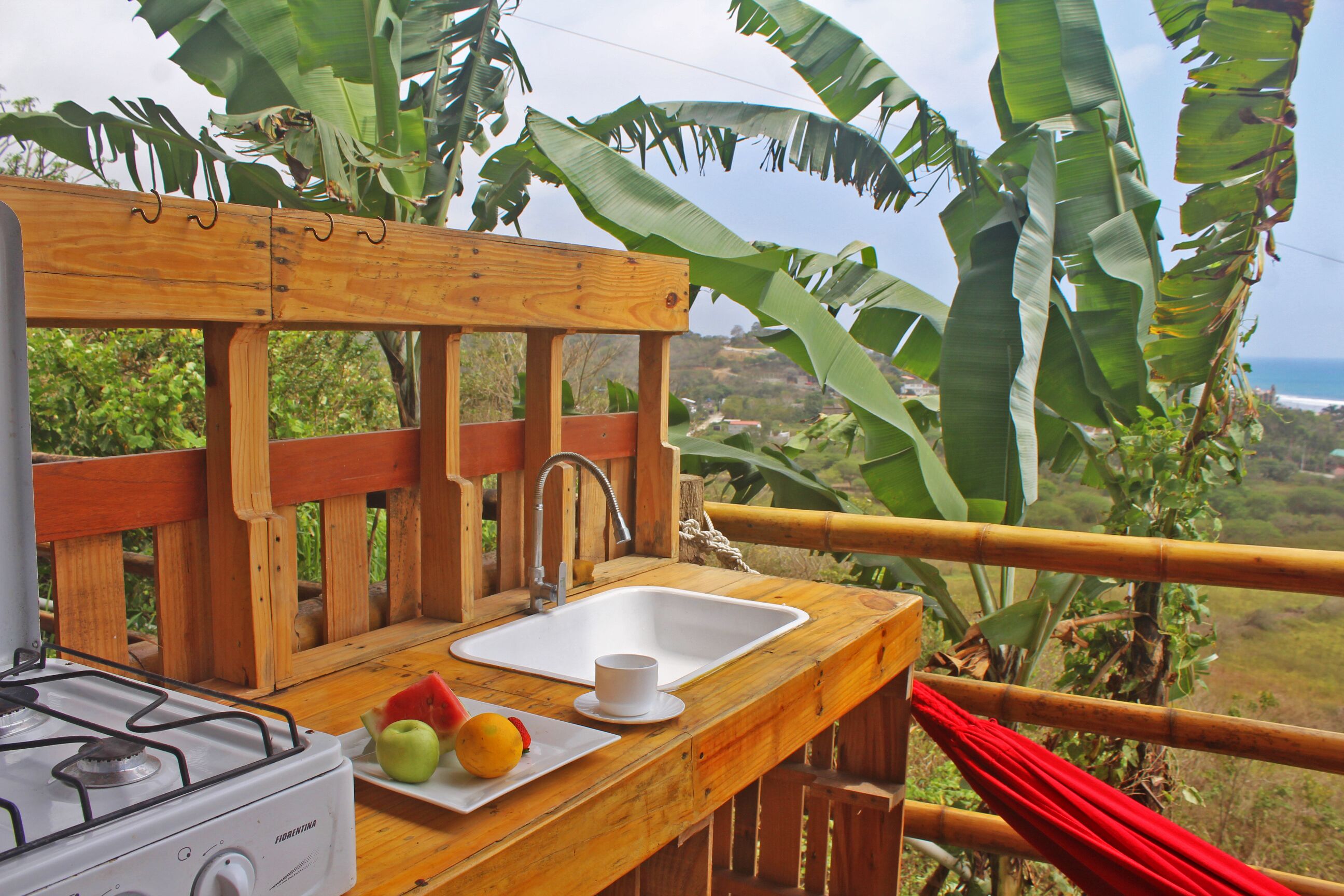 A wooden outdoor kitchen with a gas stove, sink, and a plate with fruits.