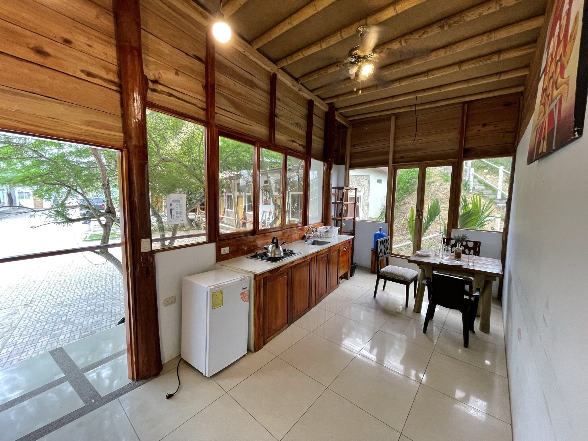 Una cocina con vigas de madera, un refrigerador, un lavamanos y un comedor con mesa y sillas.