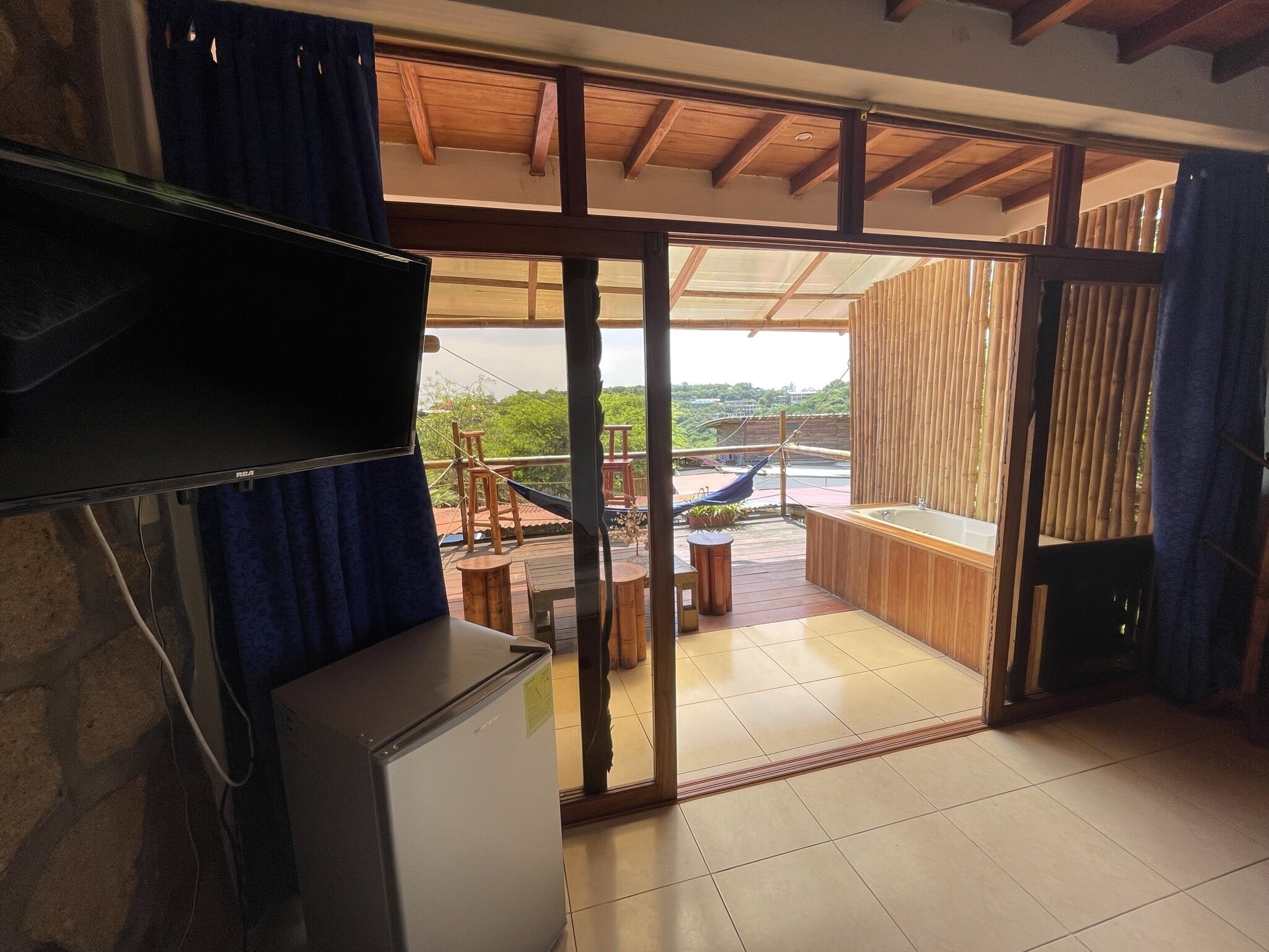 A room with a sliding glass door leading to an outdoor deck with a hammock, wooden furniture, and a view of greenery.
