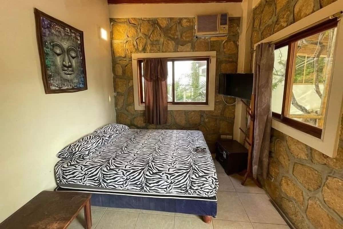 Une chambre à coucher avec un lit à motifs zébrés, un mur en pierre, une fenêtre avec des rideaux et un téléviseur fixé au mur.