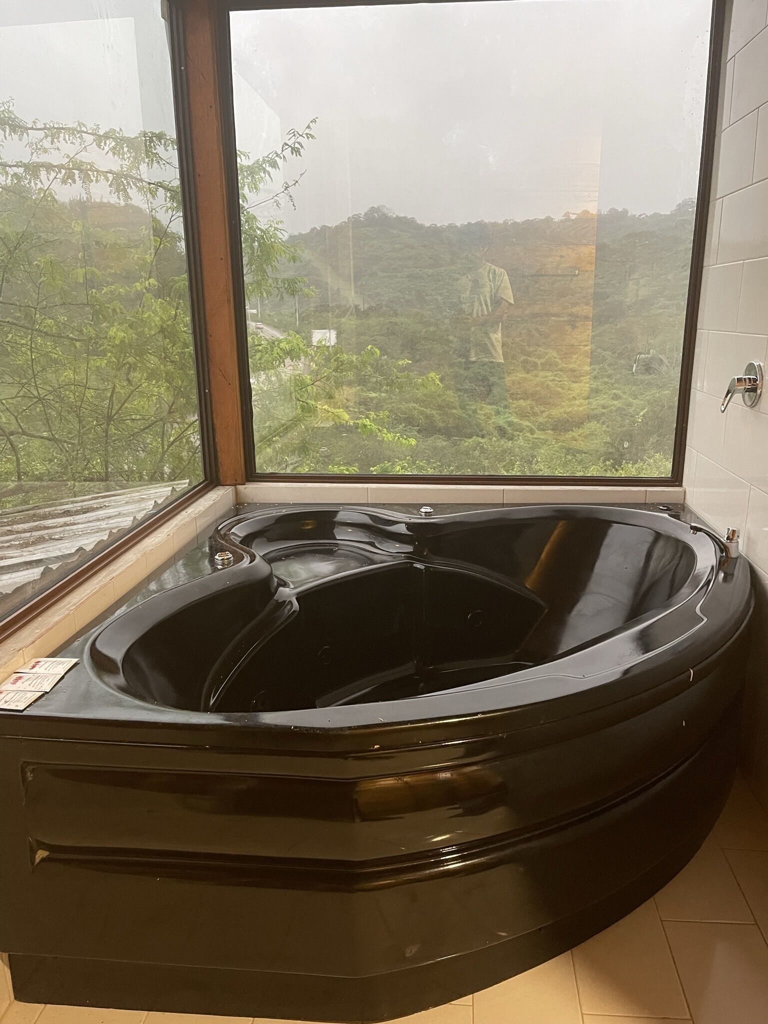 A black hot tub in a corner with a large window overlooking a green landscape.