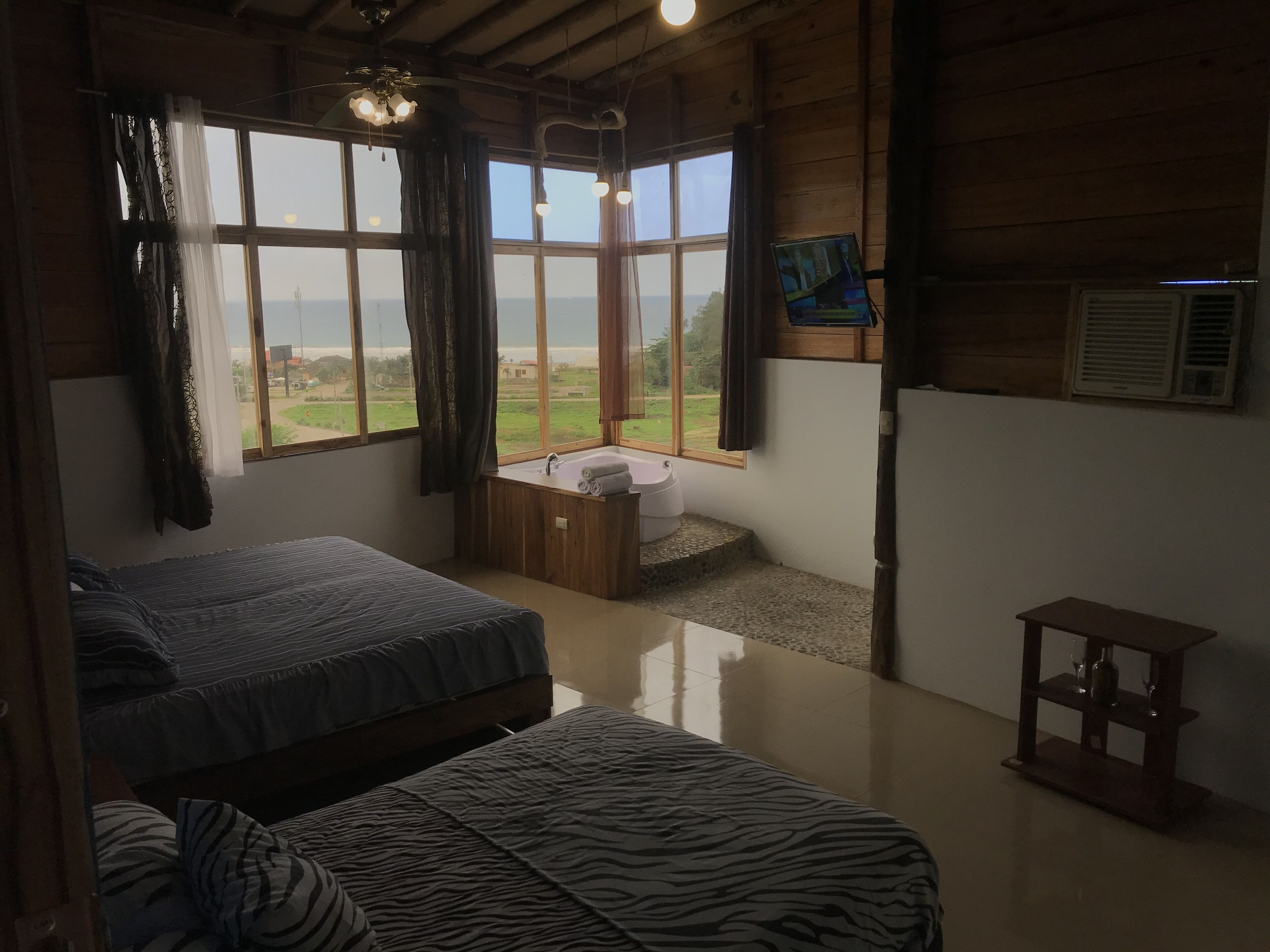 Una habitación con dos camas, una ventana con cortinas, un lavamanos y una mesita.
