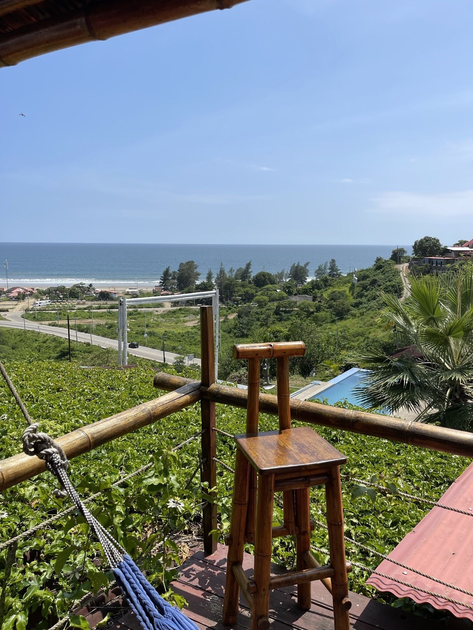 A wooden chair and hammock on a balcony overlooking a beach and ocean.