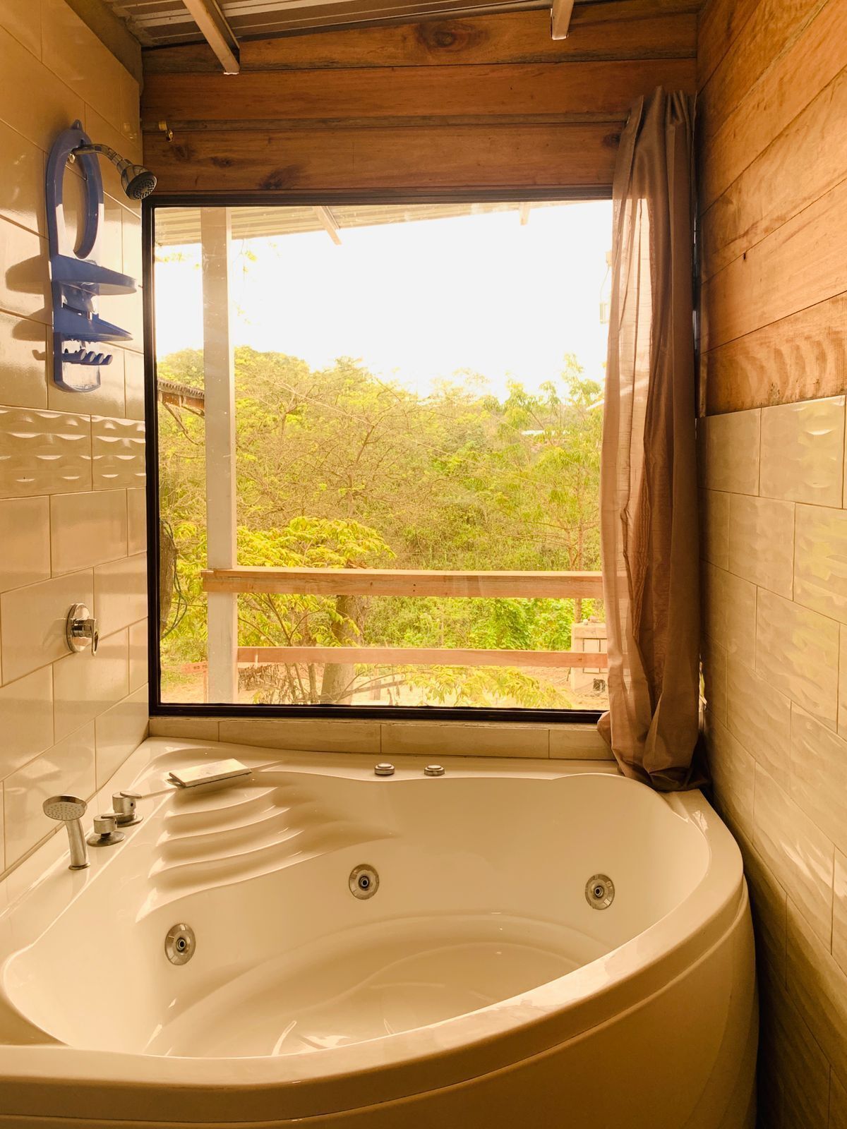 Un baño con una bañera grande, ducha y ventana con vistas a la vegetación.