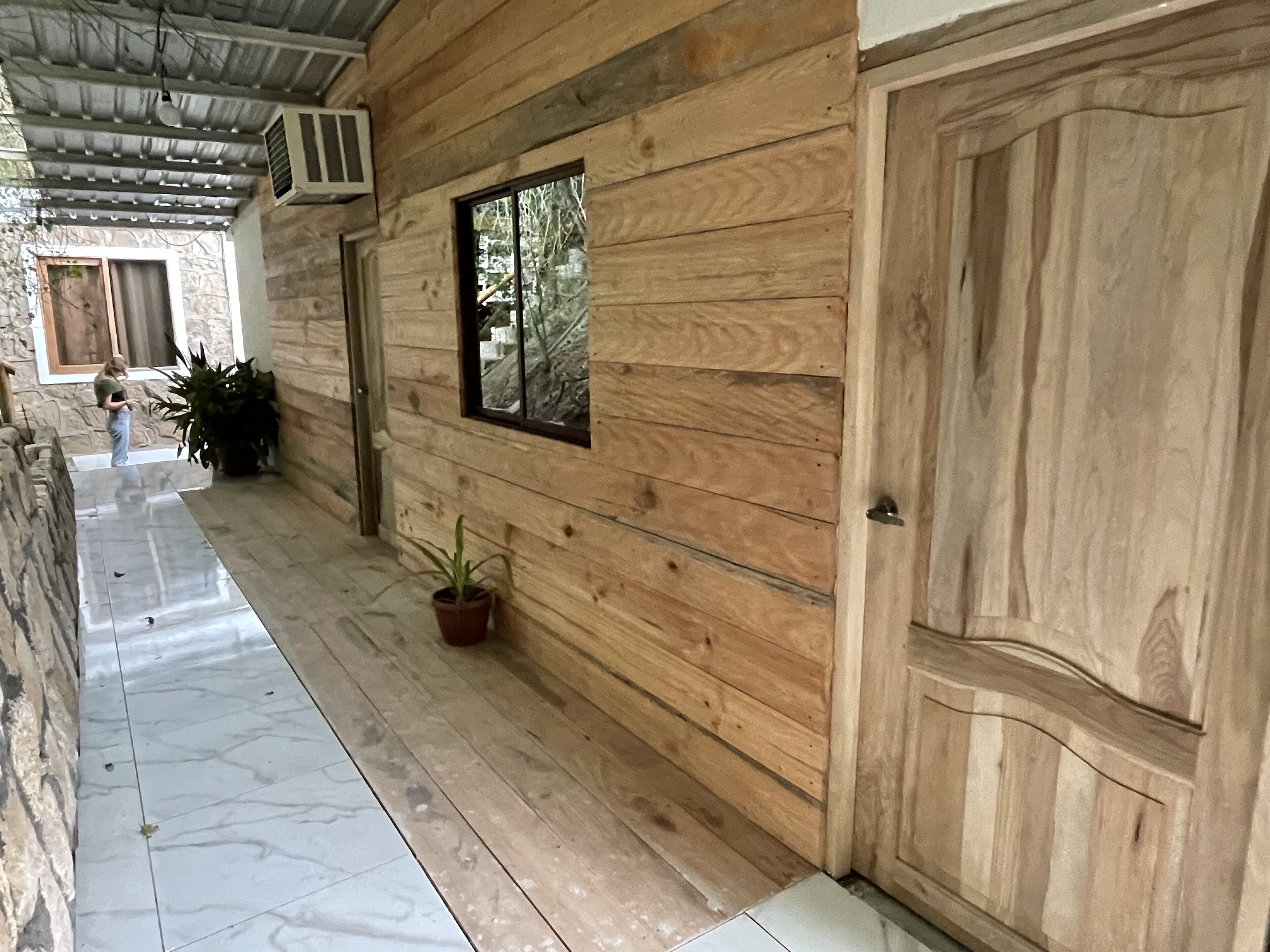 A corridor with wooden walls, a tiled floor, a potted plant, and a door.