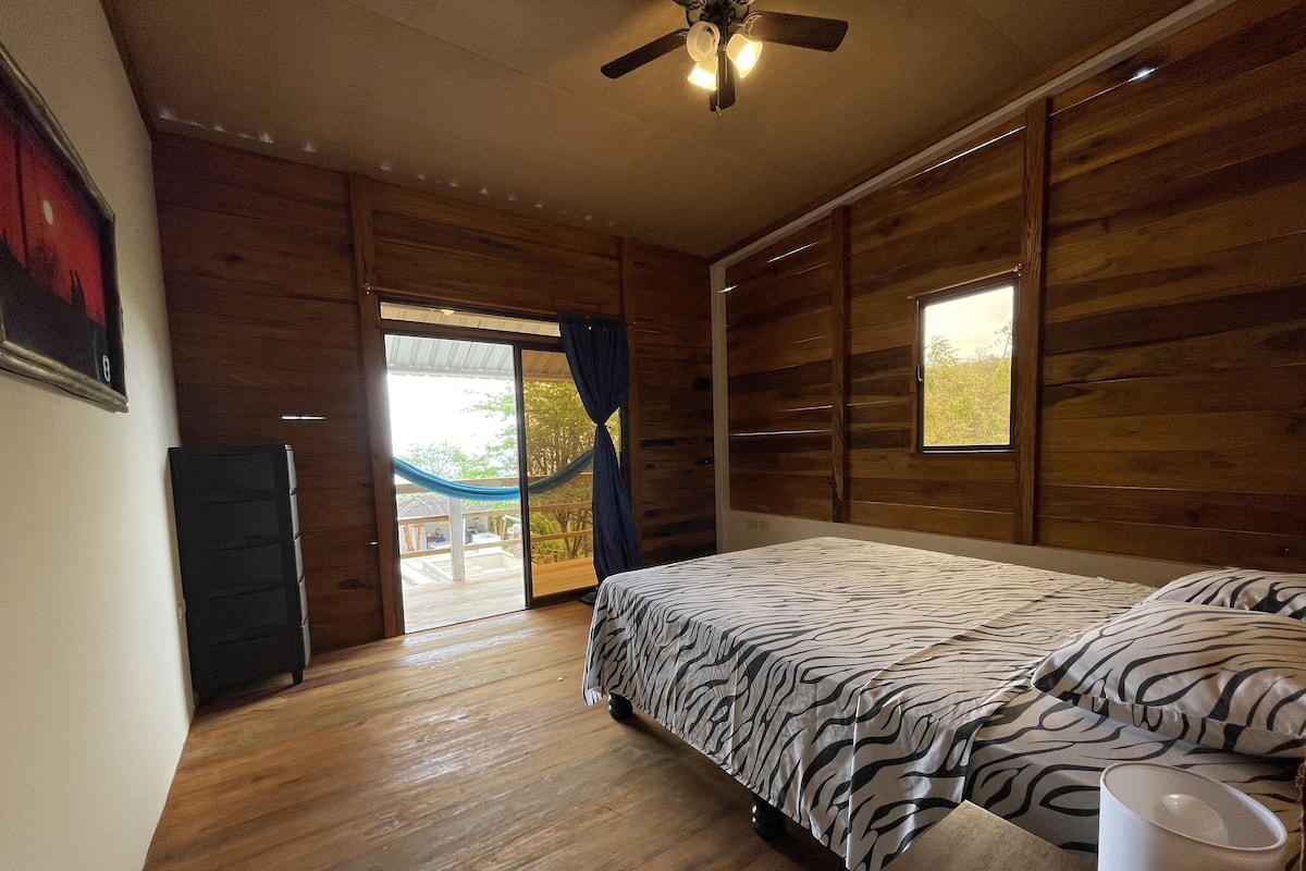 Une chambre à coucher comprenant un lit, un ventilateur de plafond, une fenêtre et une porte donnant sur un espace extérieur.