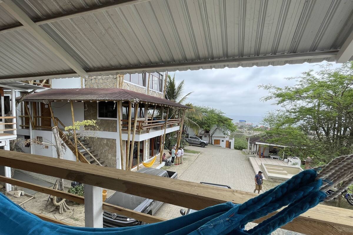 Une vue depuis un balcon donnant sur un bâtiment à la façade en pierre, avec une terrasse en bois et un hamac.