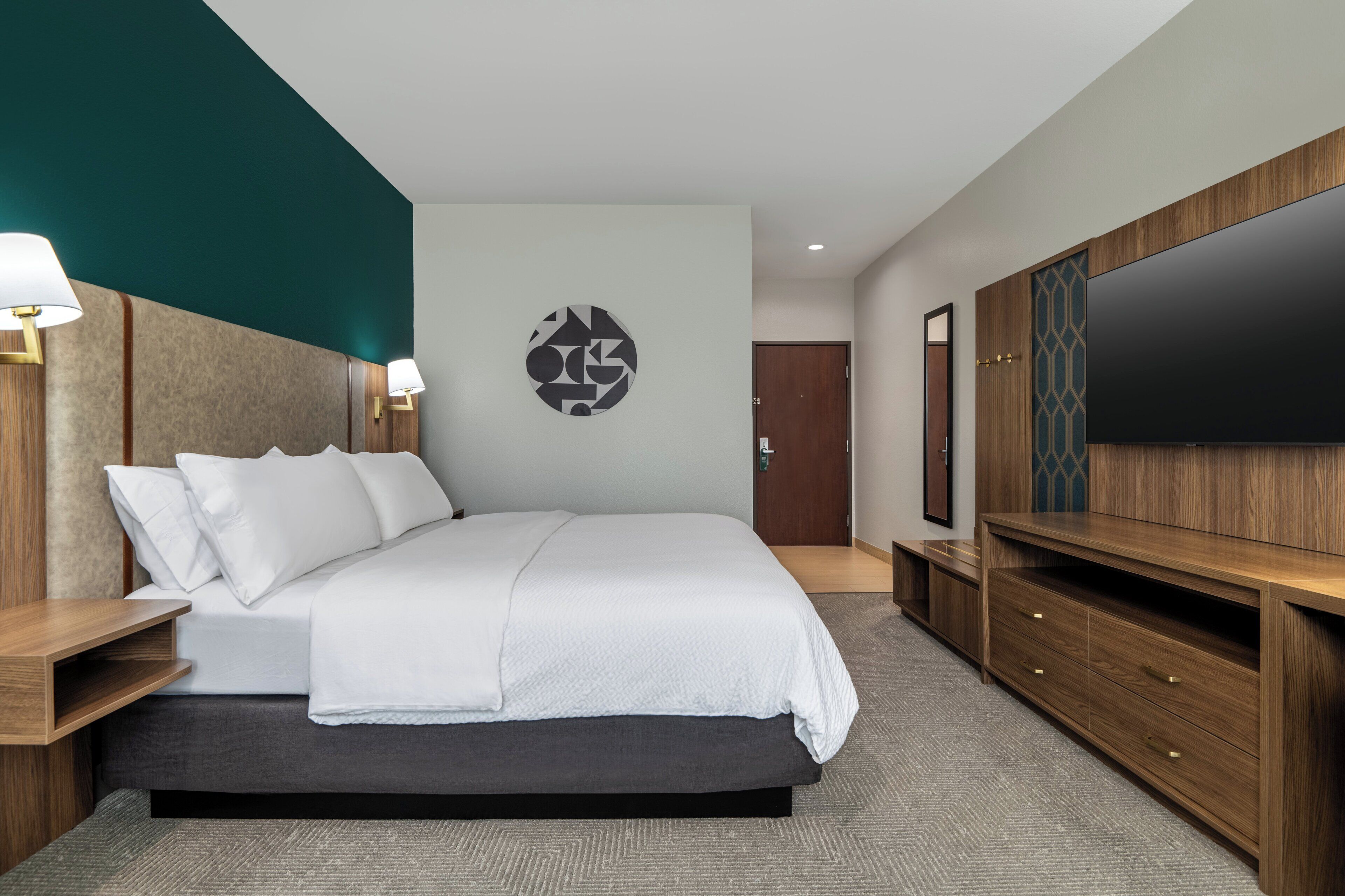 Ein modernes Hotelzimmer mit einem großen Bett, einem Holz-Kopfteil, einem Flachbildfernseher und einer eingebauten Holzkommode.