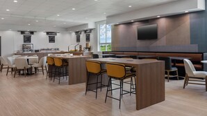 Un restaurante moderno con una barra central, diversas opciones de asientos y una gran pantalla de televisión en la pared.