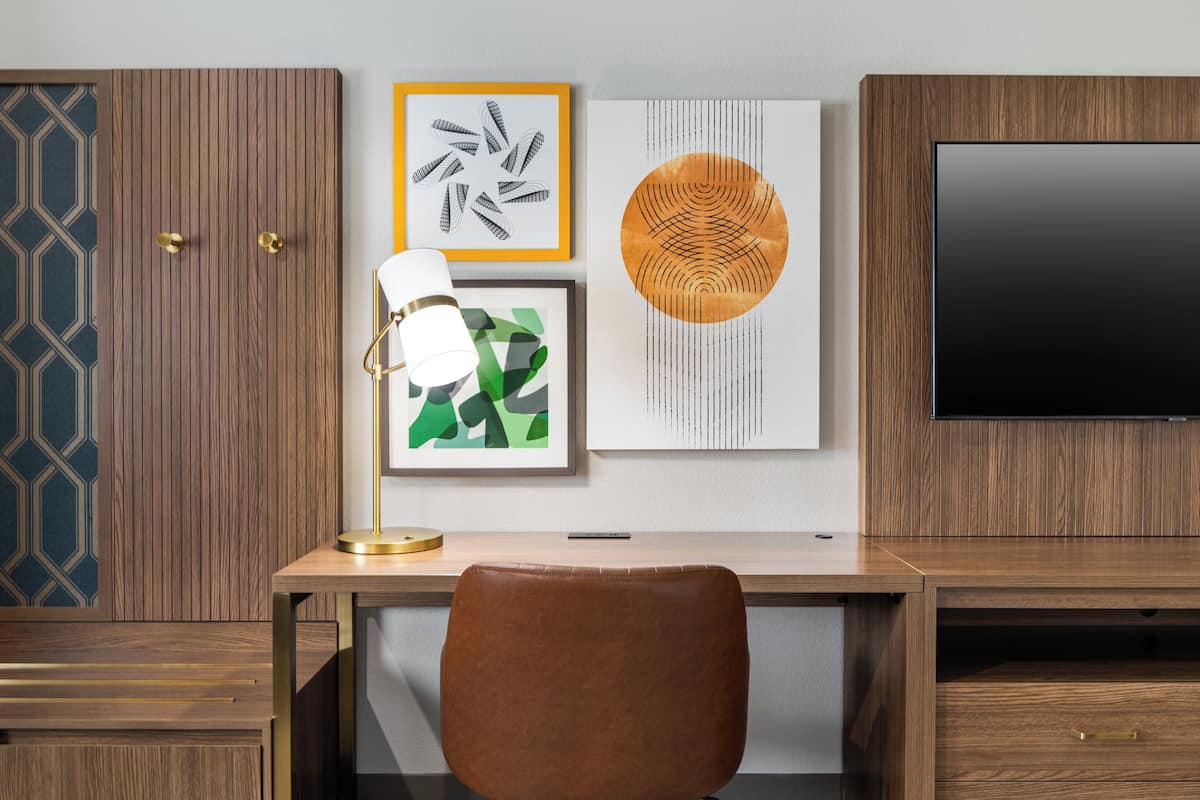 A modern office space with a wooden desk, a brown leather chair, a wall-mounted TV, and three framed artworks.