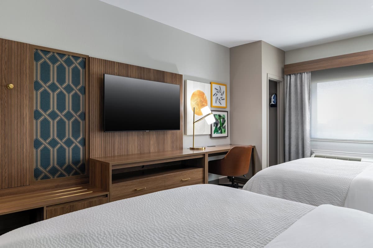 A hotel room with two beds, a TV, a desk with a chair, and artwork on the wall.