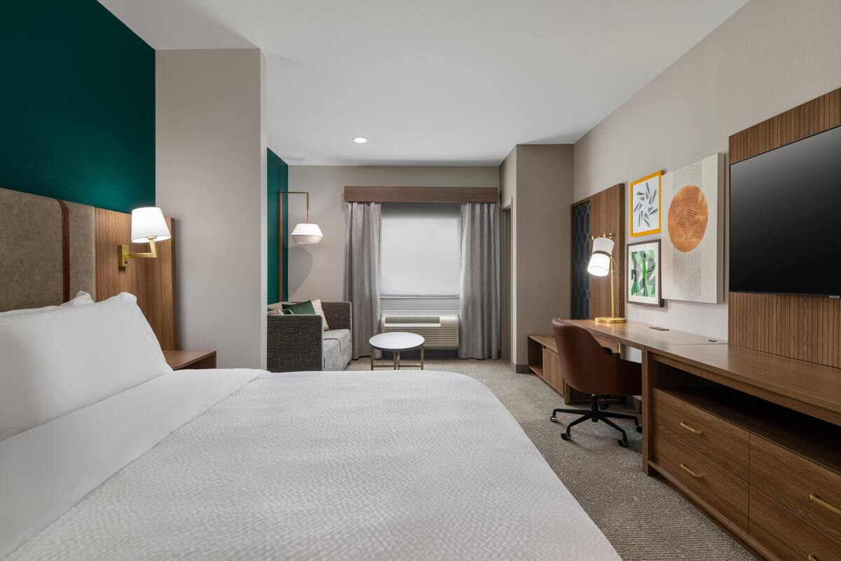 A hotel room with a bed, desk, chair, and TV.