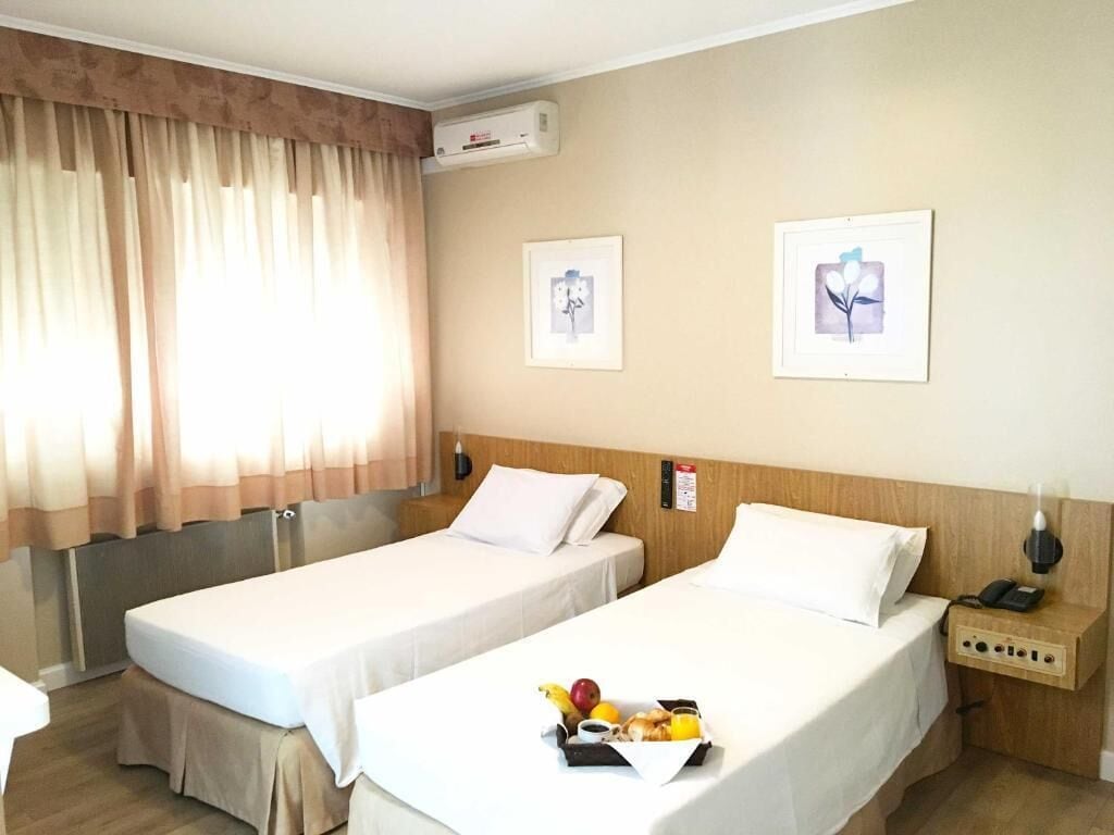 A hotel room with two beds, a bedside table with a phone, and a wall-mounted air conditioner.