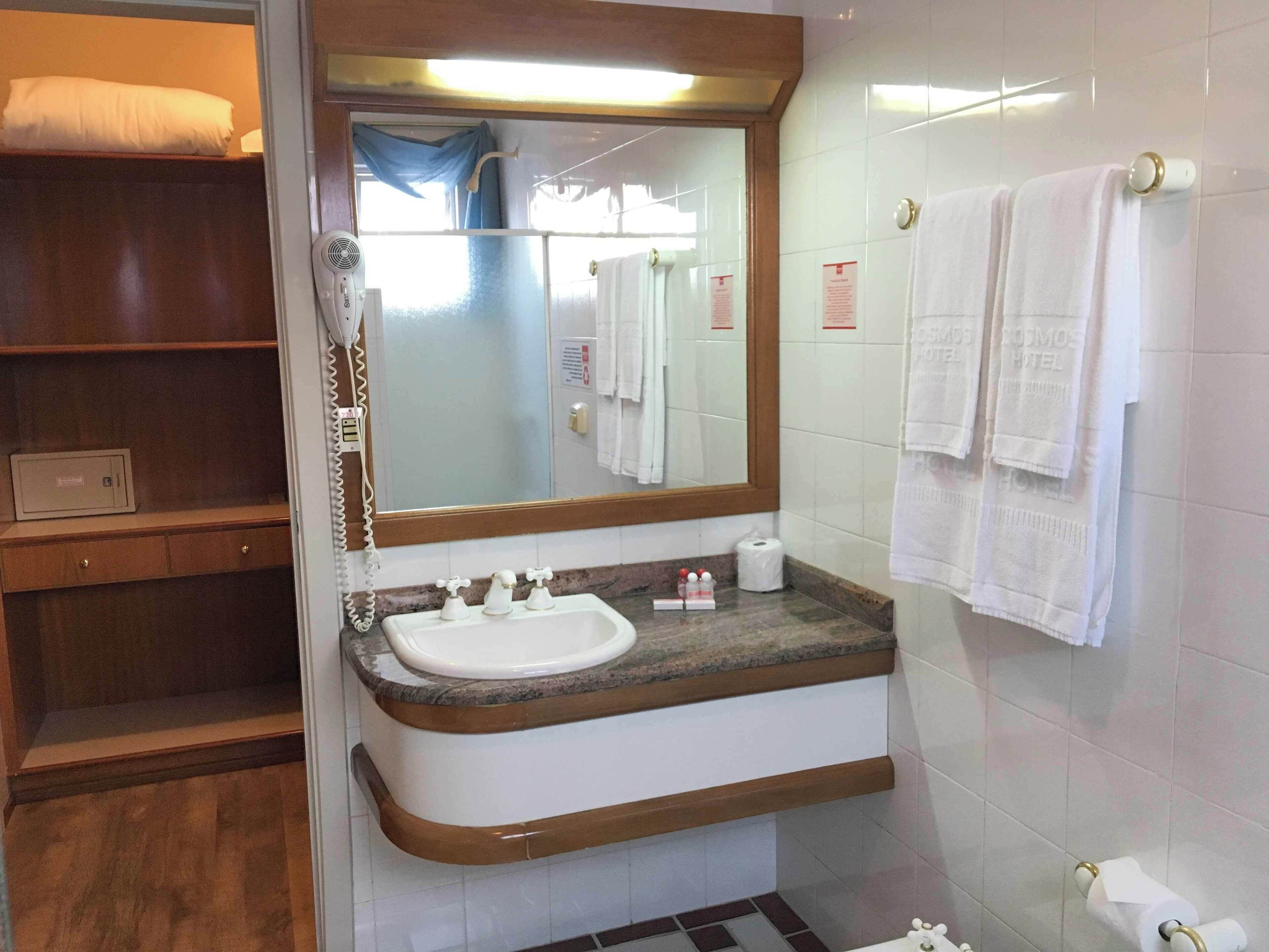 Un baño con lavamanos, espejo, toallero y estante de madera.