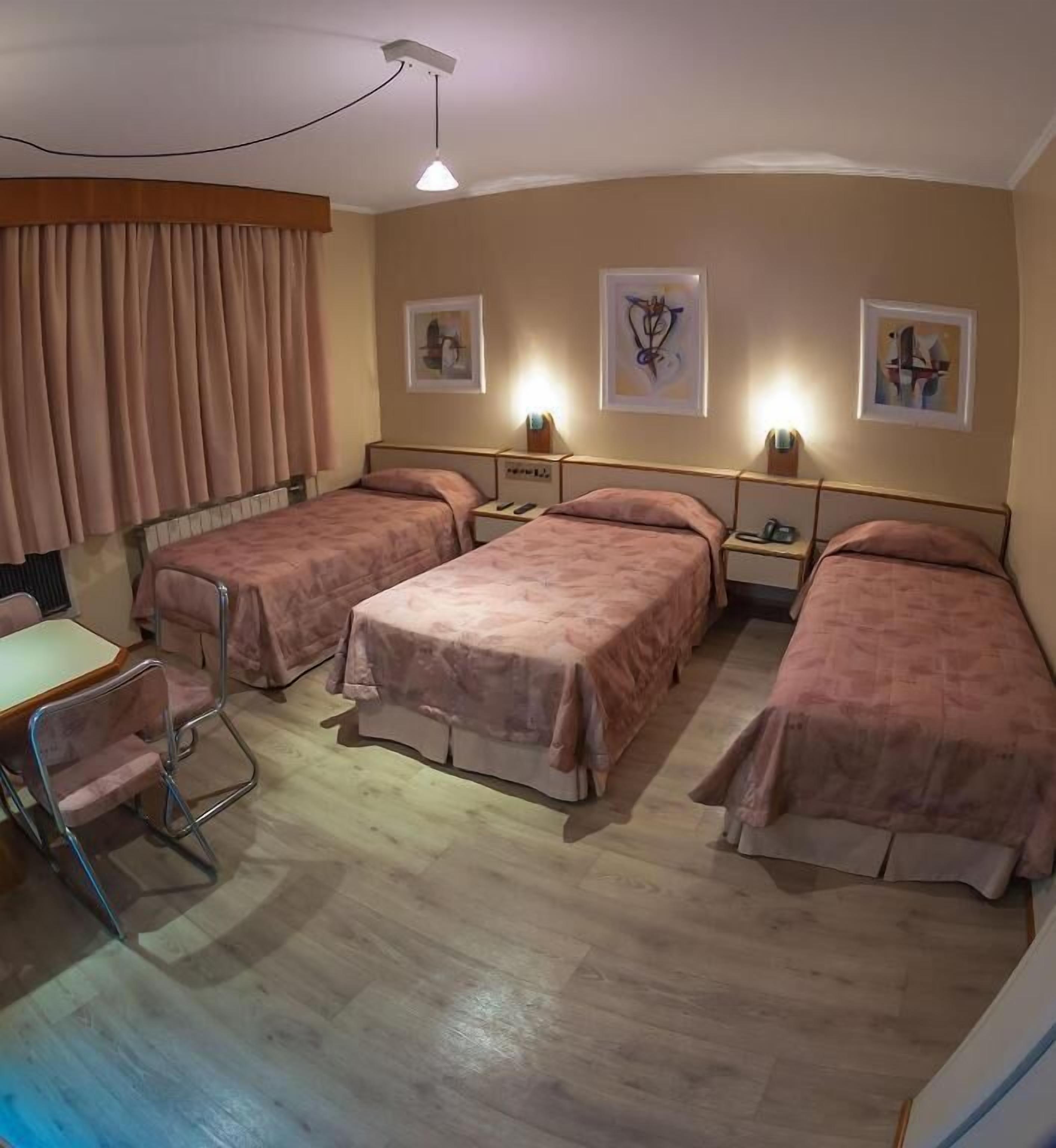 A hotel room with four beds, a desk, and a chair.
