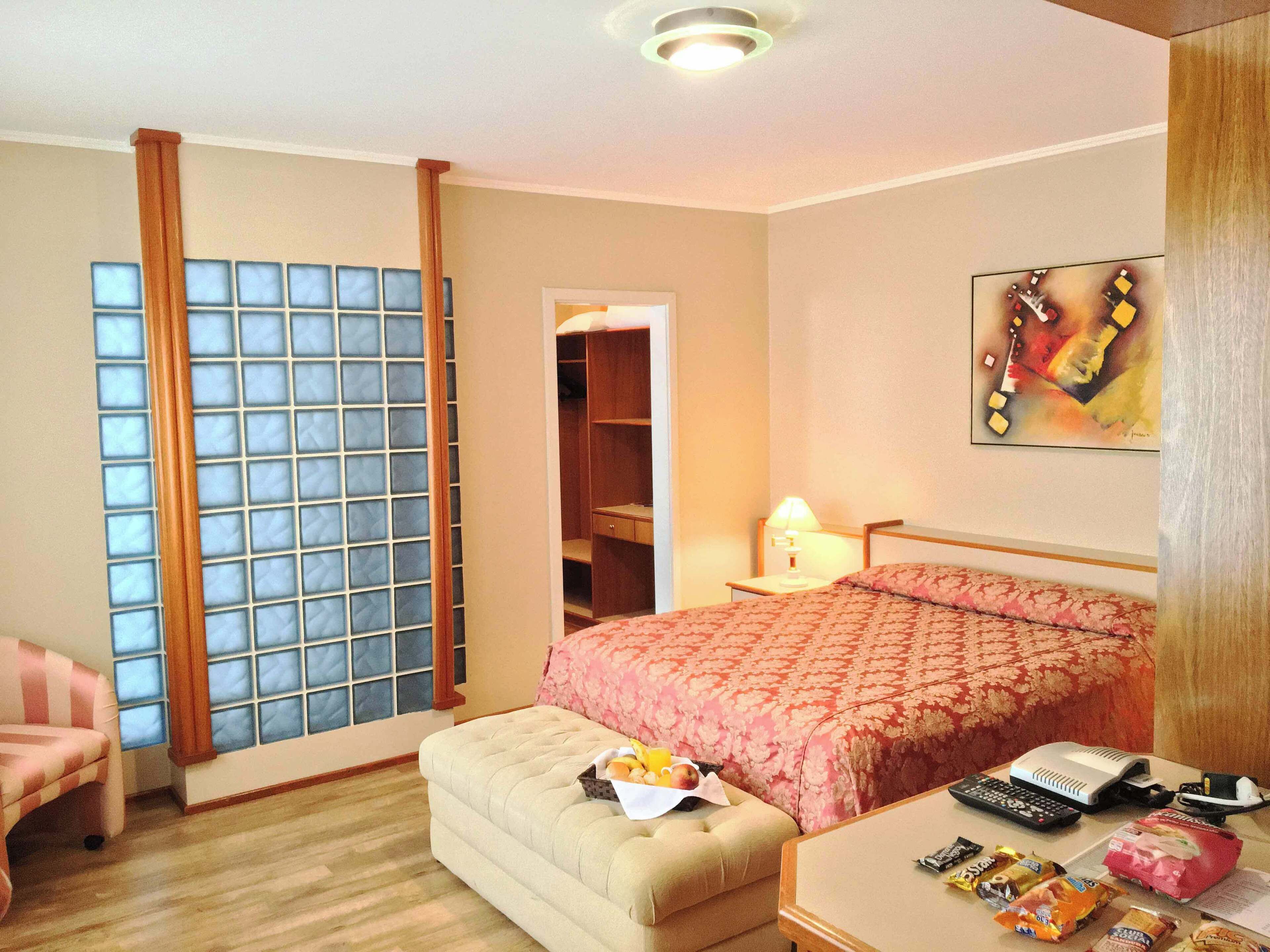 Ein Hotelzimmer mit einem Bett, einem Schreibtisch mit Lampe, einem Sessel und einem Fenster mit Vorhängen.