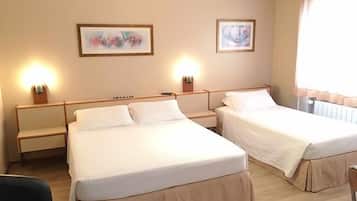 Habitación de hotel con dos camas individuales, cabecero de madera, mesita de noche con lámpara y dos cuadros enmarcados en la pared.