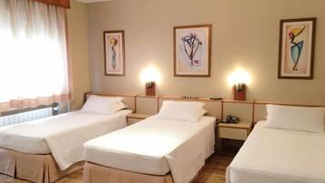 A hotel room with three single beds, wooden headboards, bedside tables, and artwork on the walls.