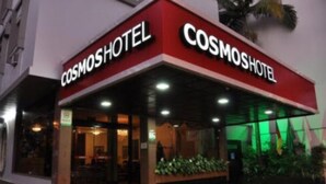 The exterior of the Cosmos Hotel with a red and white facade, large glass windows, and a green-lit entrance area. - Cosmos Hotel (Caxias do Sul)